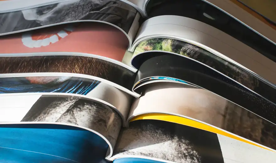 Opened printed magazines fanned out, showing vibrant full-colour pages